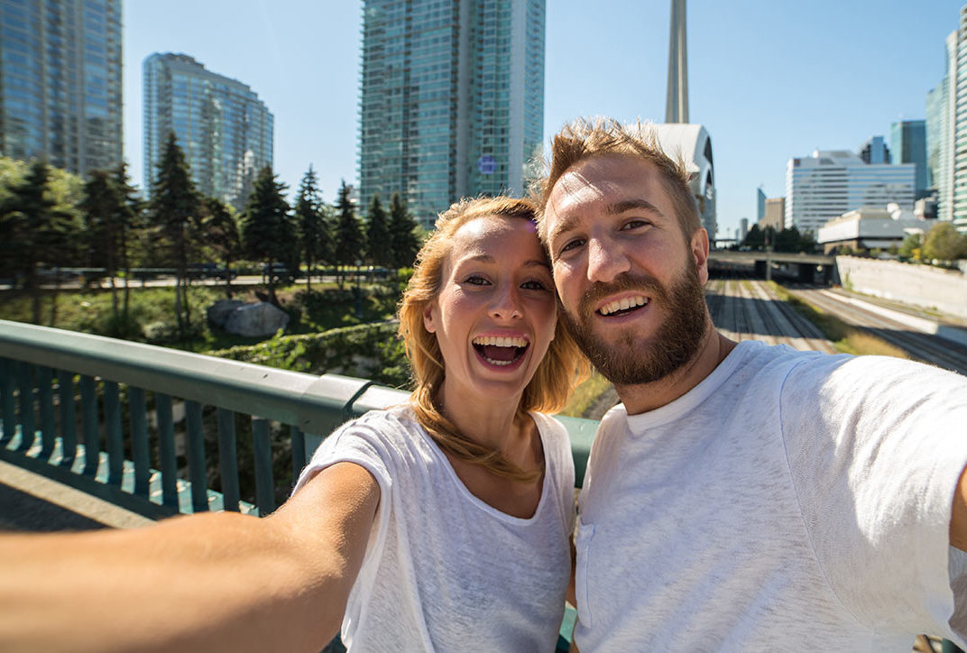 Happy couple taking a selfie in front of the CN Tower in Toronto